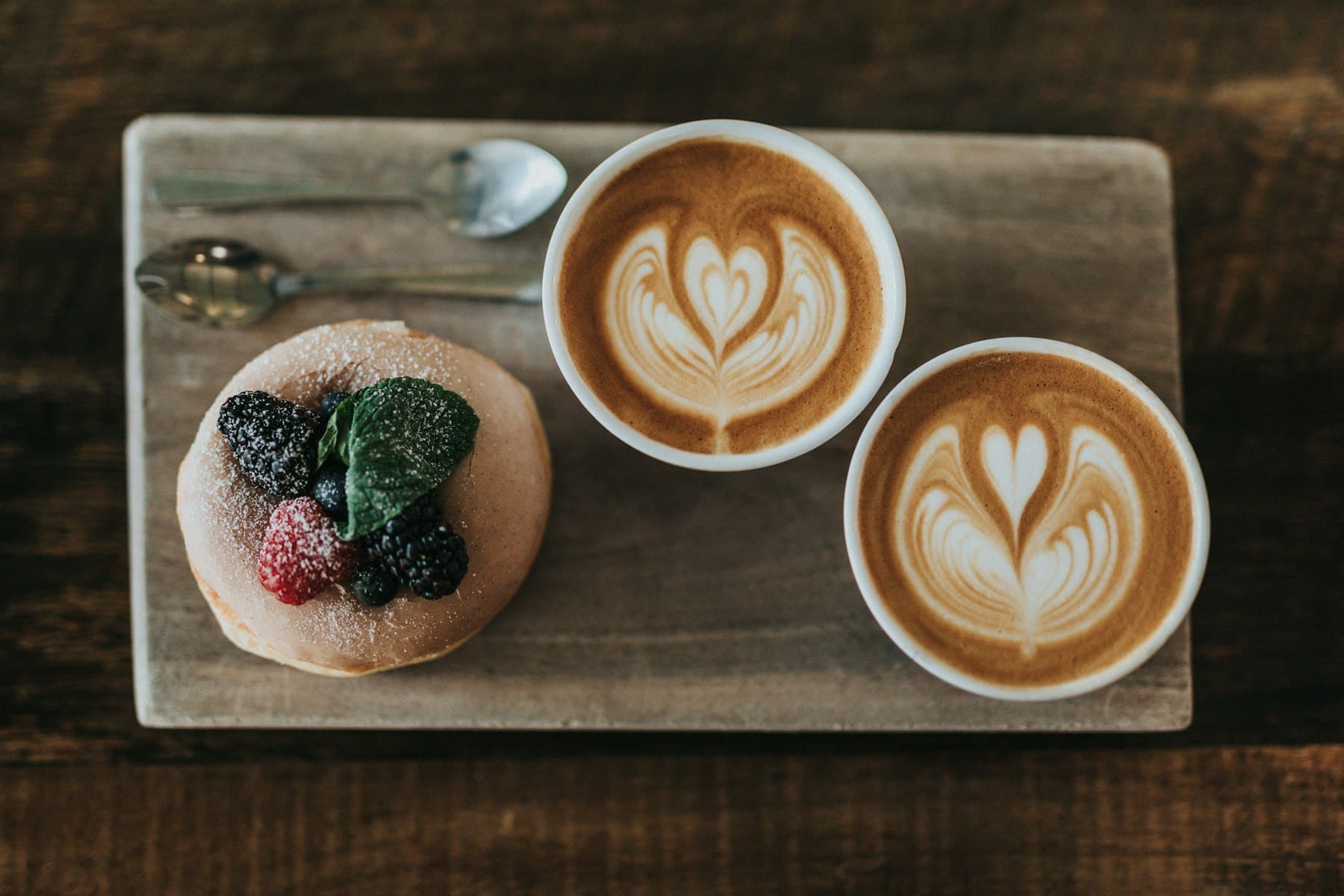 Two cappuccinos with latte art on a wooden serving board
